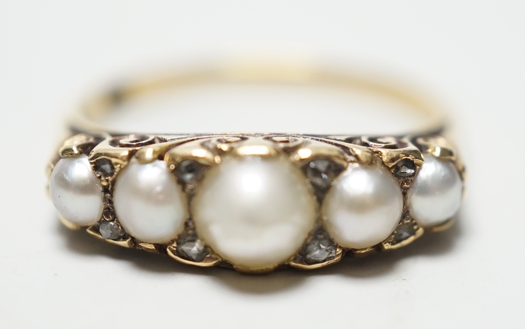 A late Victorian yellow metal (stamped 18) and five stone graduated split pearl set half hoop ring, with diamond chip spacers, size O, gross weight 2.8 grams.